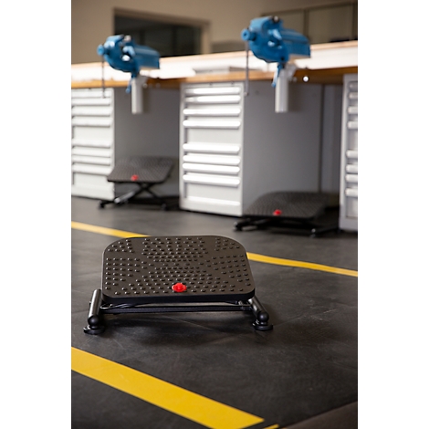 Black footrest with studs, red button and metal feet, on yellow marked floor.