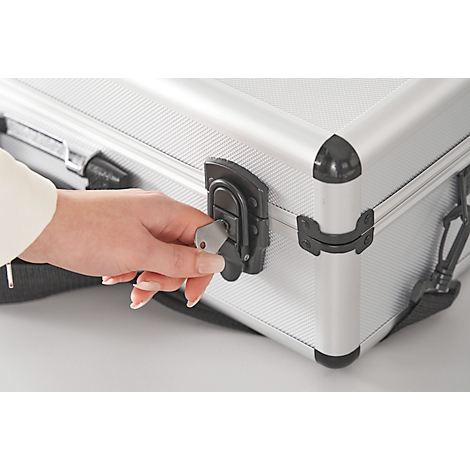 A hand locks a silver suitcase with a key.
