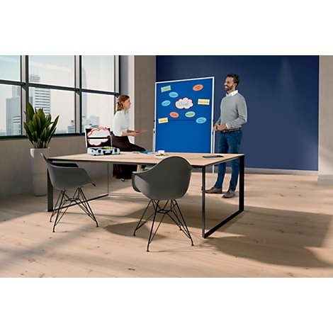 Twee mensen staan voor een blauw prikbord. Er staat een doos op de tafel en twee stoelen ervoor.