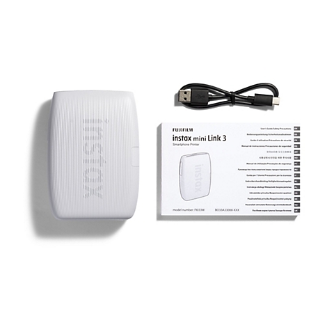 Auf weißem Hintergrund liegen eine weiße Instax Mini Link 3 Smartphone Drucker, ein Ladekabel und eine Broschüre.