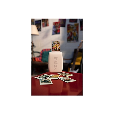 Rosafarbener Instax-Drucker, der ein Foto ausdruckt. Darunter liegen ausgedruckte Fotos auf einem roten Tisch.