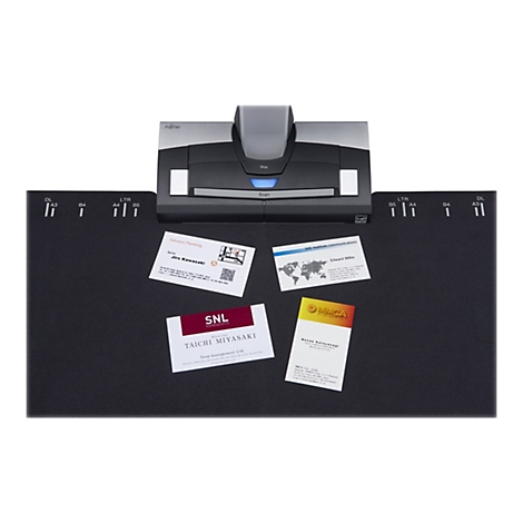 Un scanner Fujitsu gris avec trois cartes de visite sur un tapis noir. Le scanner est doté d'un bouton de numérisation, d'une lumière bleue et du mot "Fujitsu". Les cartes de visite ont des designs différents et sont étiquetées.