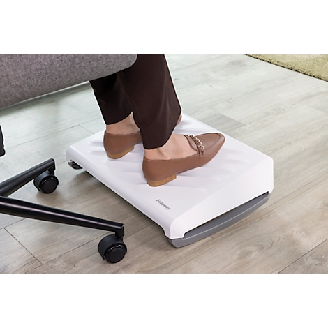 Füße ruhen auf einer weißen Fußstütze mit braunen Schuhen. Aufschrift: Fellowes.