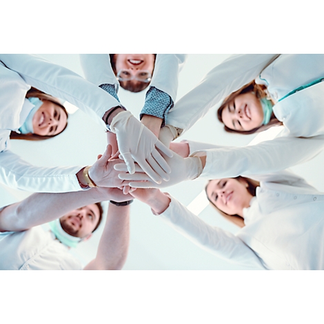 Équipe médicale en cercle, mains jointes, en blouses blanches et gants, souriant.