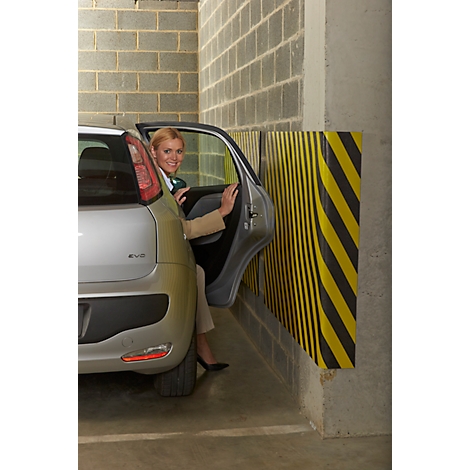 Woman entering a silver car, next to a wall with yellow and black stripes. Concrete walls in the background.