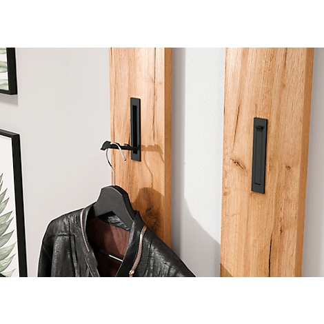 Holzgarderobe an weißer Wand. An einer schwarzen Halterung hängt eine schwarze Lederjacke. Rechts daneben weitere Halterung.