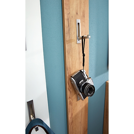 Kamera hängt an Holzlatte, die an blauer Wand befestigt ist. Haken aus Metall.