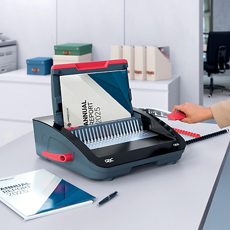 Een grijze bindmachine met rode accenten bindt een jaarverslag. Daarnaast ligt een gebonden rapport en een pen.