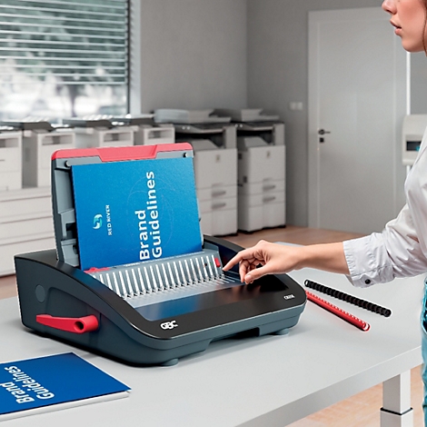 Een persoon die documenten bindt in een zwart en rood bindmachine. Op het blauw-witte boek staat 'Brand Guidelines'.