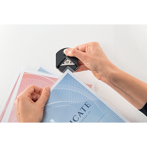 Handen die hoeken afronden van papier met blauwe en rode achtergronden. Een hoeksnijder wordt bediend.