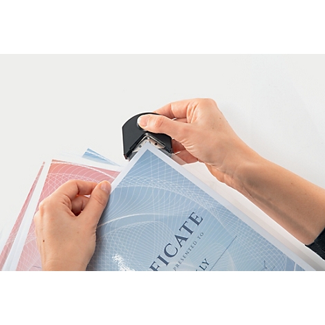 Mains coupant les coins d'un certificat avec un arrondisseur d'angles noir. Papiers en arrière-plan.