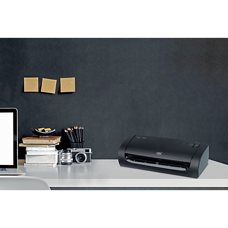 Laminateur noir sur un bureau blanc avec ordinateur portable, stylos et notes.