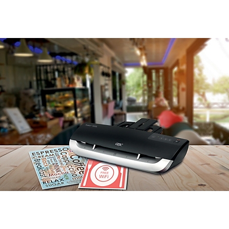 Ein Laminiergerät auf einem Holztisch in einem Café. Auf dem Tisch liegen laminierte Schilder, darunter ein Kaffee-Menü und ein "WiFi"-Zeichen.