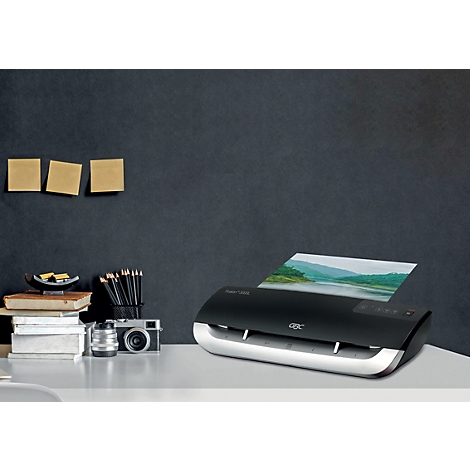 Ein schwarzes Laminiergerät mit silbernen Akzenten, das ein laminiertes Landschaftsfoto ausgibt. Auf dem Tisch liegen weitere Büroartikel.