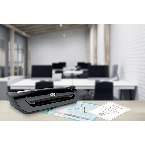 Une plastifieuse noire de la marque GBC sur un bureau. Un bureau avec des ordinateurs et des documents en arrière-plan.