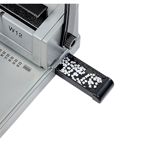 Close-up van een zilveren bindmachine. De zwarte opvangbak bevat witte plastic onderdelen.