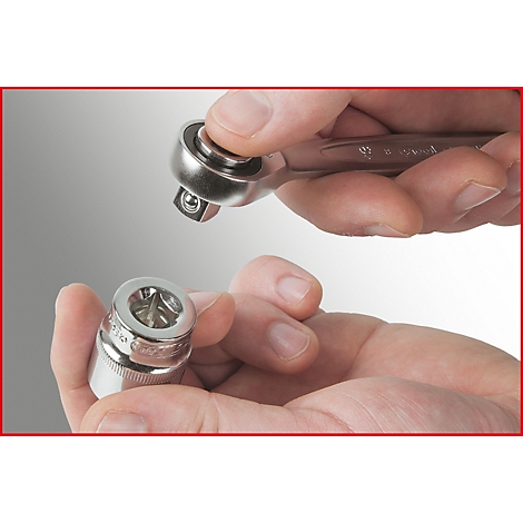 Nahaufnahme von Händen, die eine Ratsche und eine Stecknuss halten. Der obere Teil der Ratsche ist in der Nähe der Stecknuss.