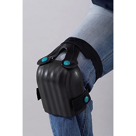 Genouillères sur une jambe. Les coussinets noirs sont fixés avec des boutons bleus et des sangles noires. Le porteur porte un jean.