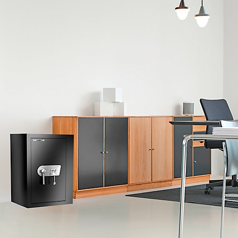 Schwarzer Tresor in einem Büro. Holzschrank und Schreibtisch im Hintergrund.