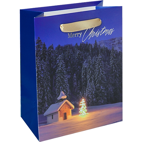 Blau-goldene Geschenktüte mit 'Merry Christmas'-Schriftzug und Winterlandschaft. Kapelle und beleuchteter Weihnachtsbaum im Schnee.