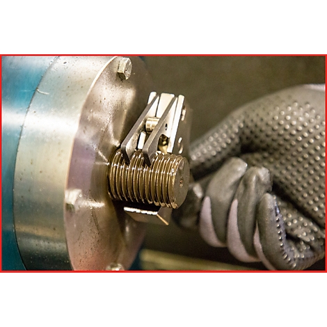 Hand mit Handschuh befestigt Schraube mit Werkzeug. Das Werkzeug ist aus Metall.