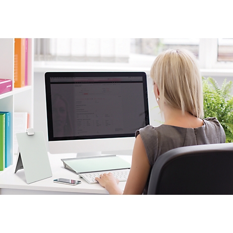 Eine Frau sitzt an einem Schreibtisch vor einem Computer. Sie tippt auf einer Tastatur. Neben ihr stehen ein Notizblock, ein Handy und eine Zimmerpflanze.