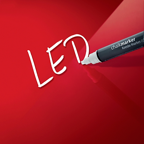Ein schwarzer Kreidemarker schreibt auf rotem Grund das Wort LED. Der Marker ist ein Chalkmarker/Kreide-Marker.