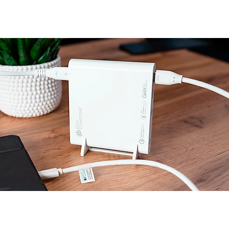 Witte oplader met USB-C-kabels die een telefoon oplaadt. Op een houten bureau. Een kleine plant op de achtergrond.