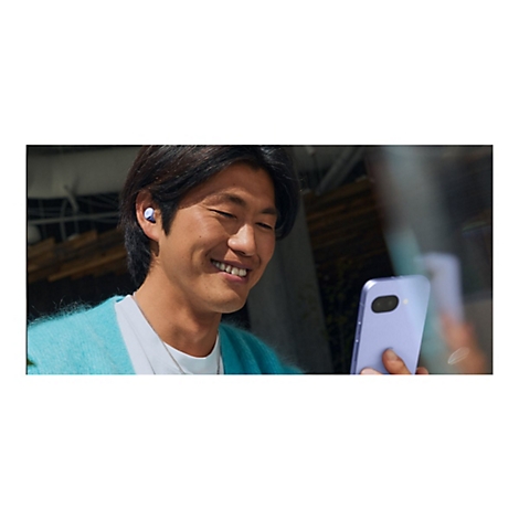 Ein Mann mit einem Ohrhörer im Ohr und einem Smartphone in der Hand, lächelt.
