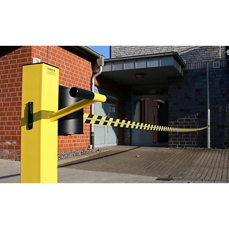 Gele slagboom met zwart-gele strepen, voor een gebouw met een rode bakstenen muur en entree.