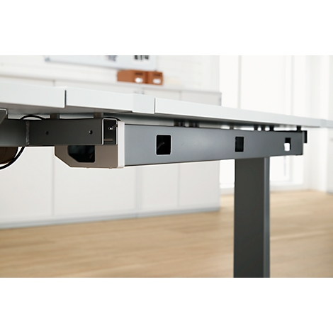 Gros plan d'un bureau réglable. Construction métallique gris-argent avec découpes. Au-dessus, un plateau de table blanc.