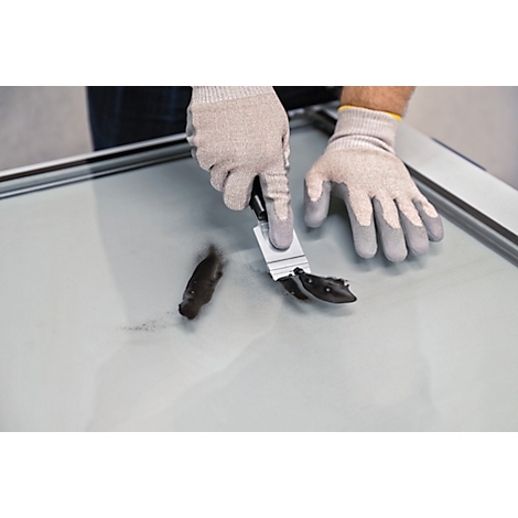 Une personne gantée retire une masse noire d'une surface lisse à l'aide d'une spatule.