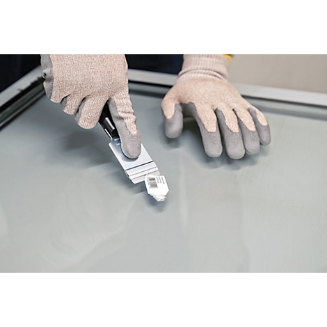 Des mains gantées tiennent un outil au-dessus d'une vitre. Un petit objet blanc est fixé à l'extrémité de l'outil.