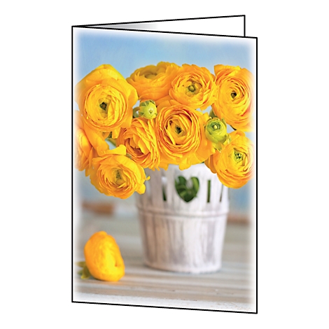 Yellow ranunculus flowers in a white, heart-shaped basket. A single bloom lies in front.