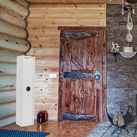 White gun safe in a wooden house. The door is made of dark wood, as is the wall behind it. On the floor stands a red vase.