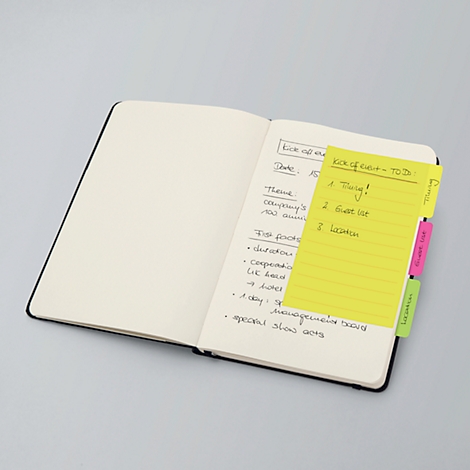 Ein offenes Notizbuch mit gelbem Zettel. Auf dem Zettel stehen Stichpunkte zu einem Thema. Das Notizbuch hat bunte Register.