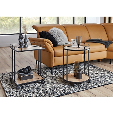 Zwei Beistelltische mit Holzplatten und schwarzen Metallrahmen vor einer braunen Couch. Auf den Tischen stehen Dekorationen.