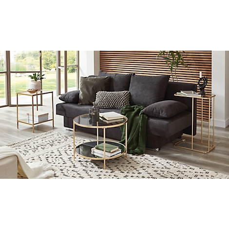 Canapé foncé avec coussins, couverture et tables d'appoint devant un mur en bois.