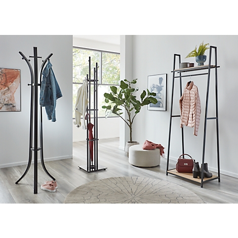 Een lichte hal met kapstokken, kleding, een plant en een rond tapijt.