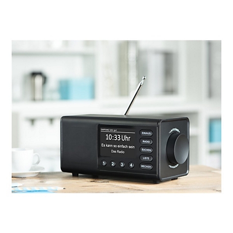 Radio noir sur une table en bois, heure 10h33, texte sur l'Ã©cran. Antenne, boutons et une commande rotative.