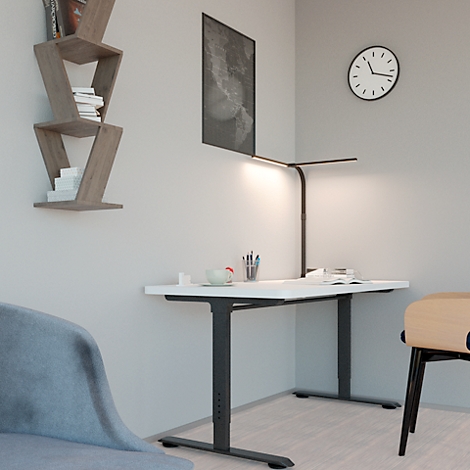 Ein heller Schreibtisch in einer Ecke, beleuchtet von einer schwarzen Lampe. Auf dem Tisch liegen Stifte, ein Becher und Notizen.