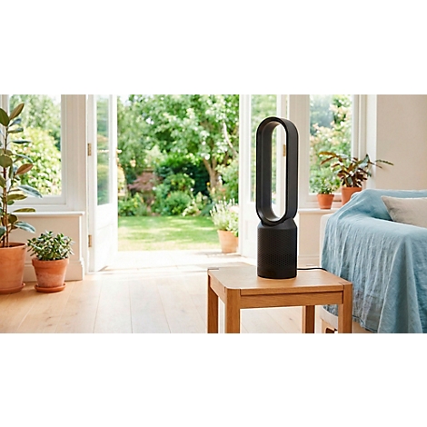 Zwarte torenventilator op houten tafel. Achtergrond: tuin, bank, planten.