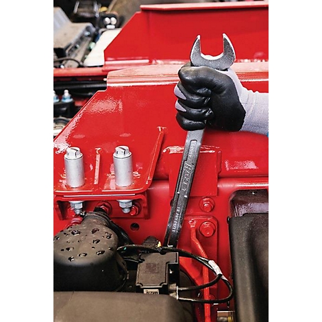 Gros plan d'une main gantée tenant une clé sur une pièce de machine rouge.