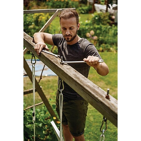 Man repareert houten frame in de tuin, met gereedschap. Groene struiken op de achtergrond.