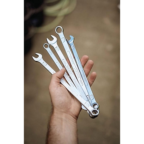 Een man die een selectie van moersleutels in zijn hand houdt. De gereedschappen zijn zilver van kleur.