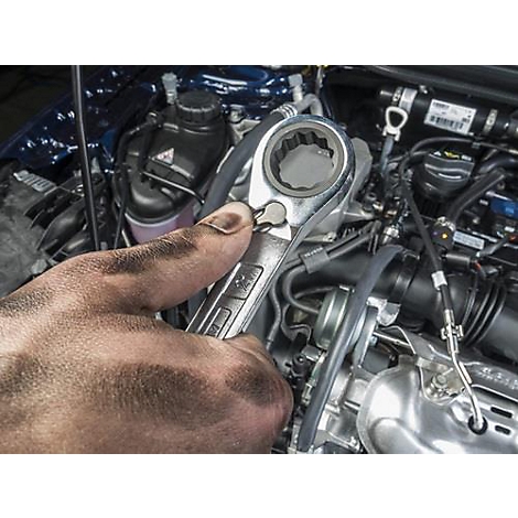 Vies hand die een sleutel vasthoudt op een automotor. Details: metaal, motor, gereedschap.