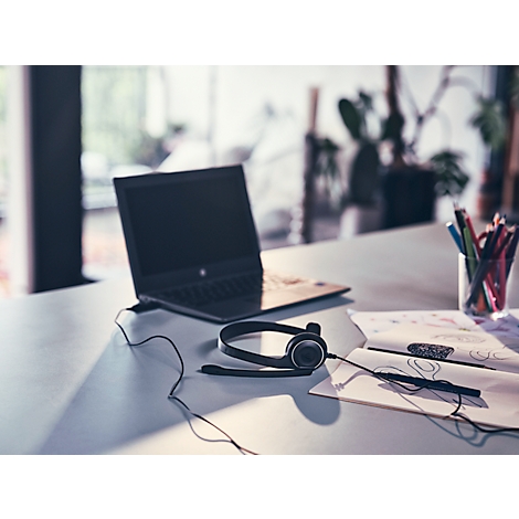 Een headset ligt voor een laptop op een tafel. Pen en notities liggen ernaast.
