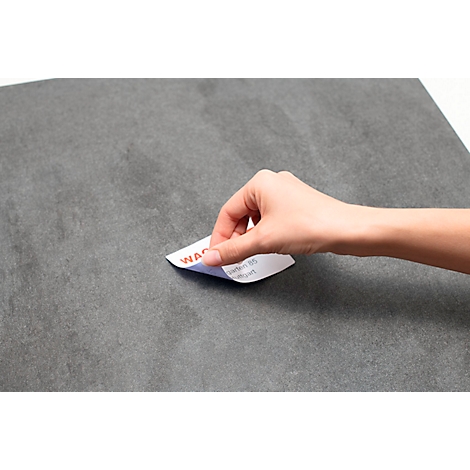 Une main soulève une étiquette avec un lettrage rouge d'une surface grise.
