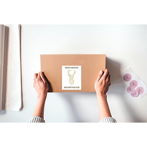 Hände halten einen Adressaufkleber mit Informationen für einen Brief. Im Hintergrund sind Umschläge und weitere Aufkleber zu sehen.