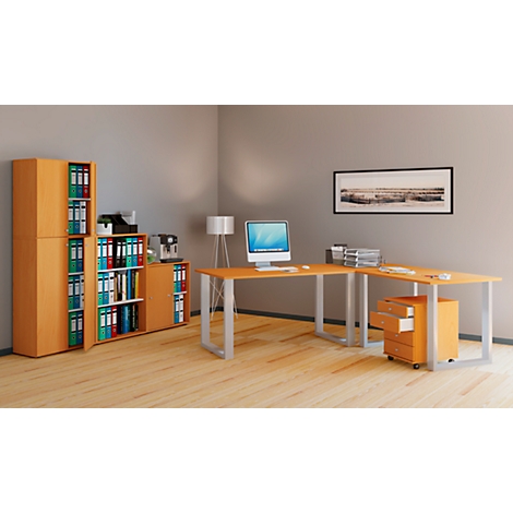 An office with wooden furniture: desk, file cabinets and mobile pedestal. On the desk are a monitor and documents, and a picture on the wall.